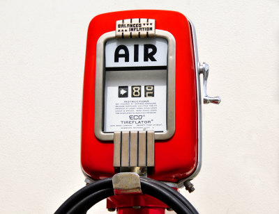 A public domain image that pictures a classic red automotive air pump with a glass enclosure for the meter and chrome accents on the housing.